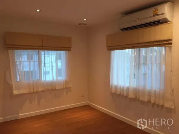 Townhouse for sale in Bang Khae, Bangkok - Bright bedroom with wood floors, two windows, beige Roman blinds and wall-mounted air conditioner.