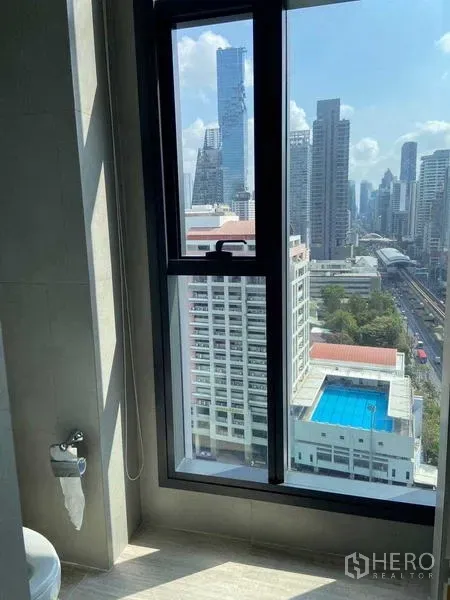 Condominium for sale in Bang Rak, Bangkok - High‑floor window view of Bangkok skyline, BTS line and a blue rooftop pool.