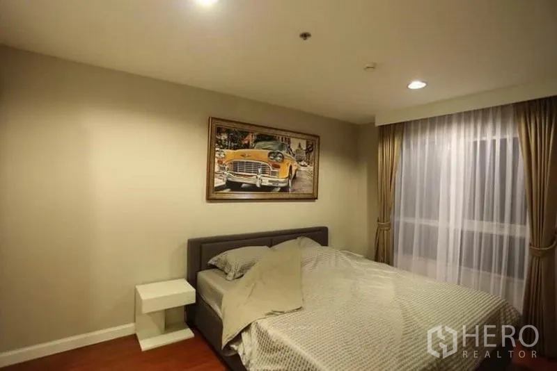 Condominium for rent in Huai Khwang, Bangkok - Master bedroom with queen bed, bedside table, drapes and framed artwork.