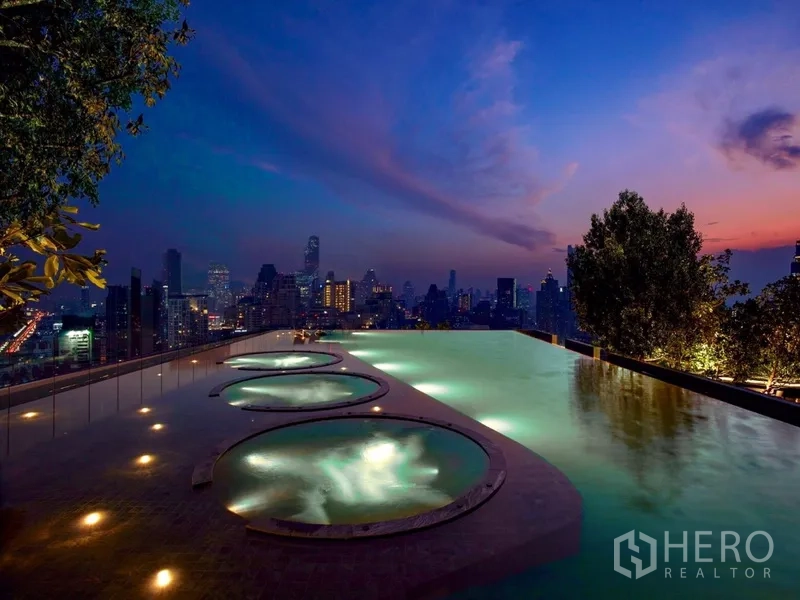 Condominium for rent or sale in Pathum Wan, Bangkok - Rooftop infinity pool at dusk with circular jacuzzis and panoramic Bangkok skyline views.