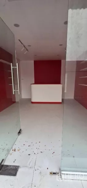 พื้นที่ขายของ for rent in Watthana, Bangkok - มุมมองผ่านประตูกระจกเต็มบานสู่พื้นที่ร้านสีแดง-ขาวพร้อมเคาน์เตอร์และชั้นวาง