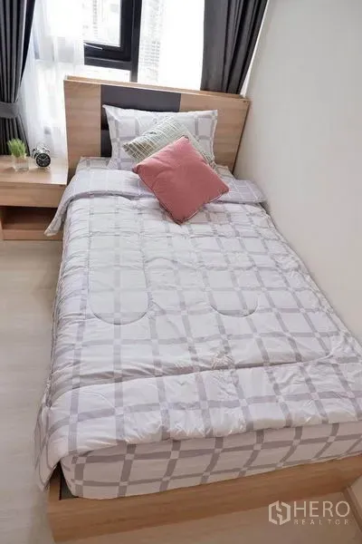 Condominium for rent in Huai Khwang, Bangkok - Second bedroom with single bed, wood headboard, and city-view window.