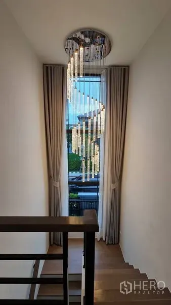 Detached House for rent in Samut Prakan - Stair landing with a tall window, full drapes and a crystal chandelier.