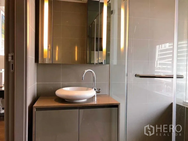 公寓 出租在Bang Rak, Bangkok - 当代风格浴室，台上盆、镜柜与玻璃淋浴间。