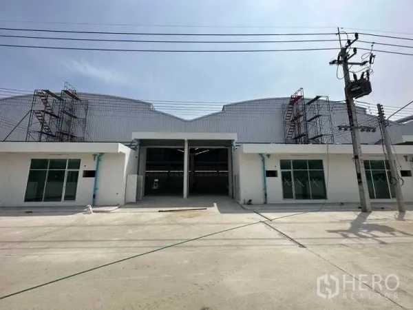 Factory for rent in Khlong Luang, Pathum Thani - Modern factory frontage with tall loading entrance, glass offices and wide concrete forecourt.