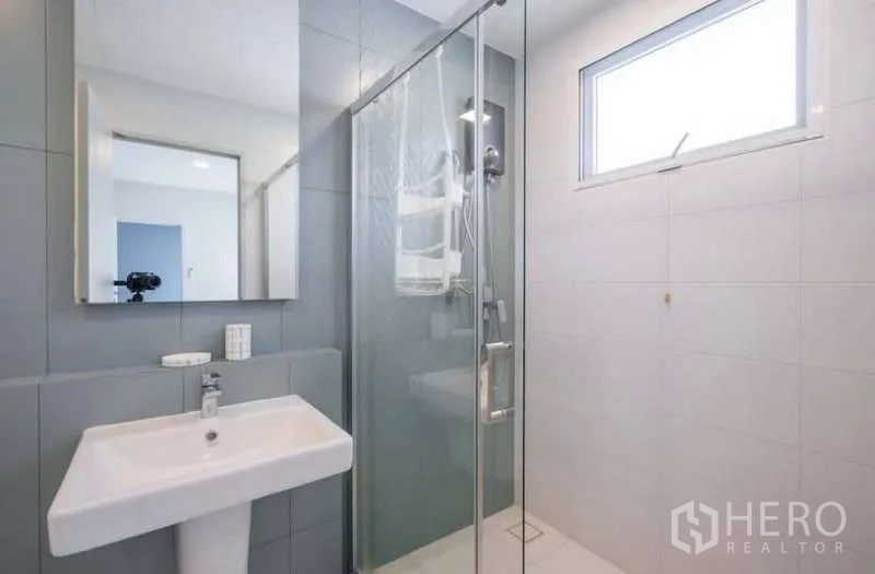 Detached House for rent in Prawet, Bangkok - Bathroom with gray tiles, pedestal sink and glass shower under a high window.