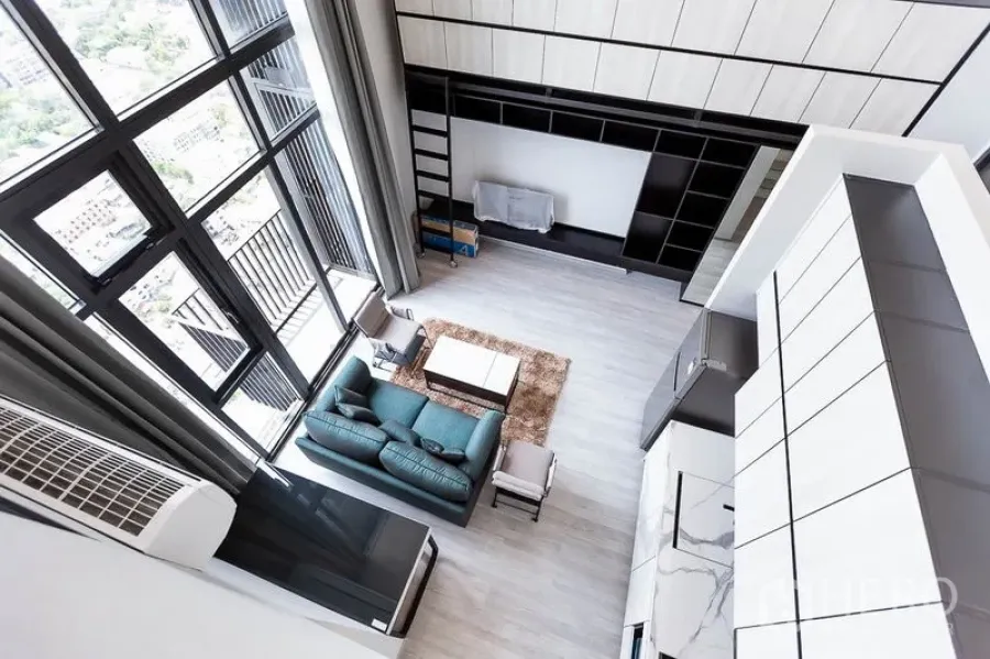 Condominium for rent in Phra Khanong, Bangkok - Double-height living room with floor-to-ceiling windows, teal sofa and built-in wall storage.