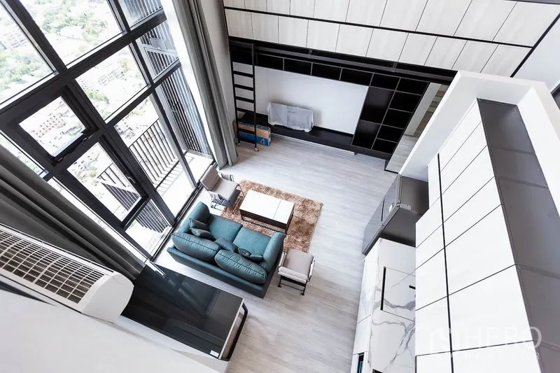 Condominium for rent in Phra Khanong, Bangkok - Double-height living room with floor-to-ceiling windows, teal sofa and built-in wall storage.