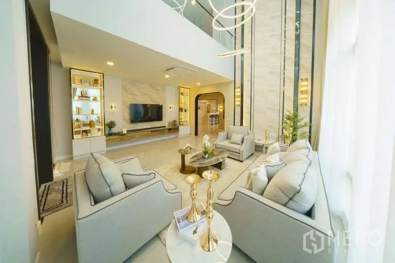 Detached House for rent or sale in Bang Phli, Samut Prakan - Stylish living area with tall feature wall, gray sofas and TV under a double-height ceiling.