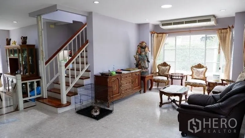 Detached House for rent in Prawet, Bangkok - Airy living room with leather sofas, large windows and a staircase.