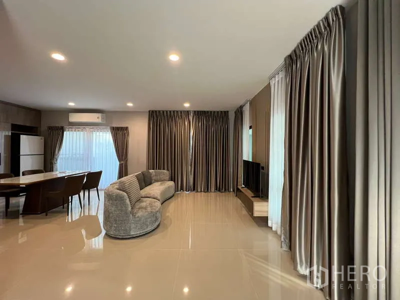 บ้าน ให้เช่าในBang Kapi, Bangkok - พื้นที่นั่งเล่นและรับประทานอาหารแบบเปิดโล่ง โซฟาโค้ง ทีวี และผ้าม่านเต็มผนัง