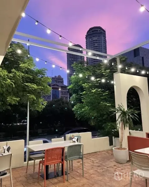 พื้นที่ขายปลีก ให้เช่าในSathon, Bangkok - เทอเรซกลางแจ้ง ประดับไฟสาย มองเห็นวิวเมืองยามเย็น พร้อมกระถางต้นไม้และเก้าอี้หลากสี