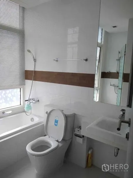 Condominium for rent in Watthana, Bangkok - Modern bathroom with bathtub, toilet, and large mirror beside a window.