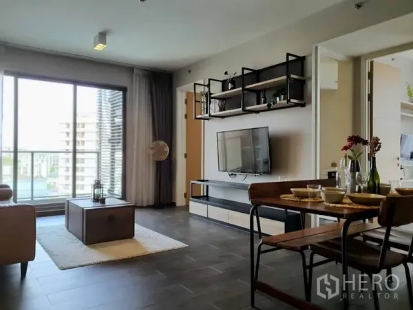 Condominium for rent or sale in Watthana, Bangkok - Sunny living area with floor-to-ceiling windows, balcony view and wall-mounted TV.