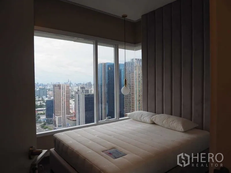 Condominium for rent in Chatuchak, Bangkok - Bedroom with floor-to-ceiling corner windows, upholstered headboard and panoramic Bangkok skyline views.