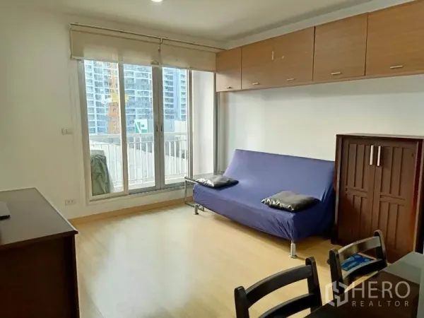 公寓 出租在Bang Rak, Bangkok - 明亮客厅，落地推拉门连通阳台，木地板与吊柜，可见城市景观。