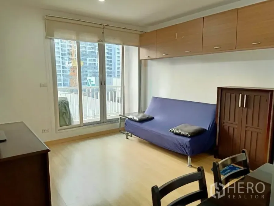 Condominium for rent in Bang Rak, Bangkok - Bright living room with sliding glass doors to a balcony, wood floors and wall cabinets overlooking the city.