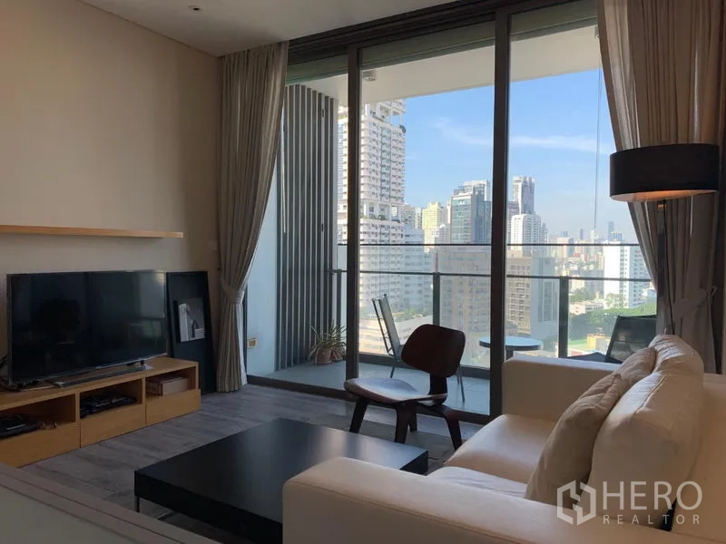Condominium for rent in Watthana, Bangkok - Bright living room with sofa, TV console and floor‑to‑ceiling glass opening to a balcony with skyline views in Watthana, Bangkok.