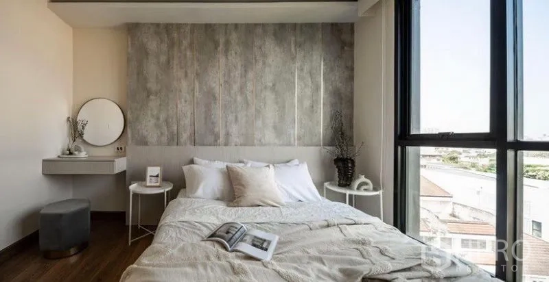 Condominium for rent or sale in Phra Khanong, Bangkok - Cozy bedroom with large window, textured feature wall, bedside tables and a small vanity corner.