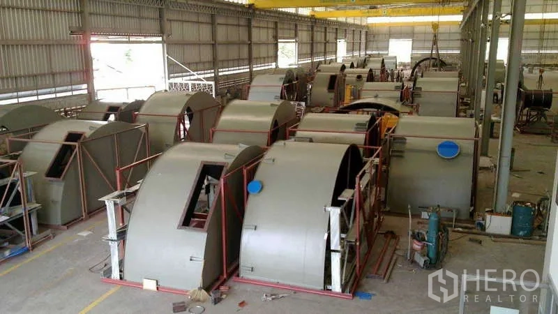 工厂 出售在Chachoengsao - 制造区摆放多组大型圆筒形金属壳体，置于框架下方有起重设备。