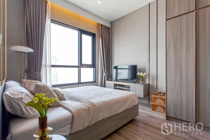Condominium for rent in Watthana, Bangkok - Primary bedroom with large window, TV console, built-in wardrobe and warm neutral tones.