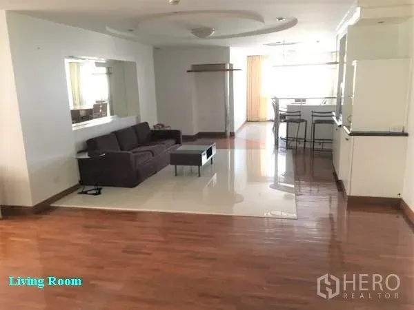 公寓 出租在Khlong Toei, Bangkok - 宽敞的开放式客厅，转角沙发、镜面墙，木地板与瓷砖地面，连接吧台。