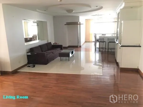 公寓 出租在Khlong Toei, Bangkok - 宽敞的开放式客厅，转角沙发、镜面墙，木地板与瓷砖地面，连接吧台。