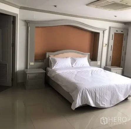 Condominium for rent in Watthana, Bangkok - Primary bedroom view with queen bed, decorative headboard, bedside tables and door to ensuite bathroom.