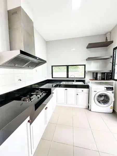 Detached House for sale in Bang Phli, Samut Prakan - Modern white kitchen with black granite countertops, gas hob, range hood and windows.