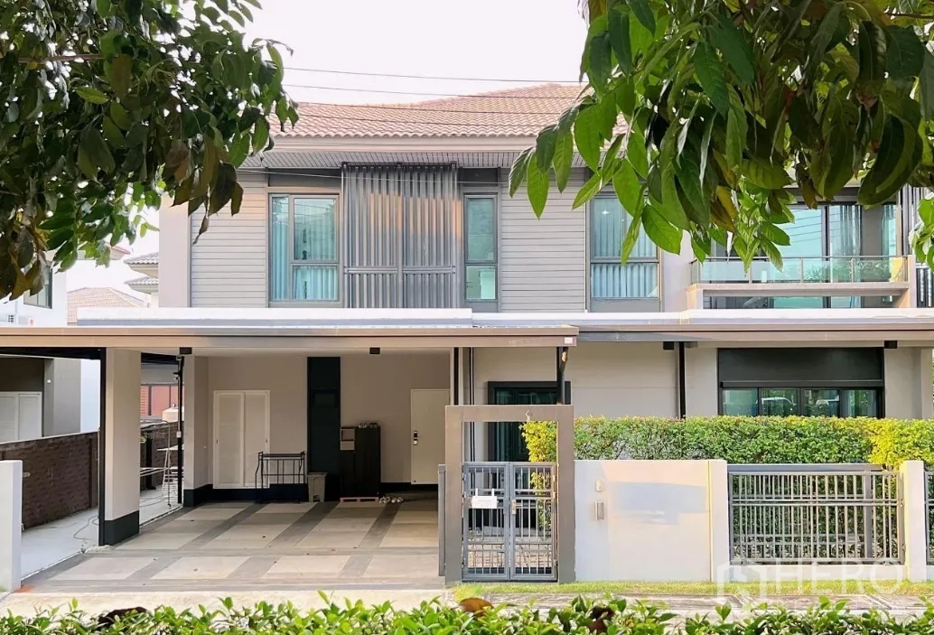 บ้าน ให้เช่าหรือขายในLam Luk Ka, Pathum Thani - ด้านหน้าบ้านพร้อมแนวรั้วพุ่มไม้ และโรงจอดรถมีหลังคายามเย็น