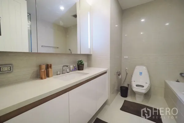 Condominium for rent in Pathum Wan, Bangkok - Modern bathroom with long vanity, mirror cabinets, toilet and bathtub.