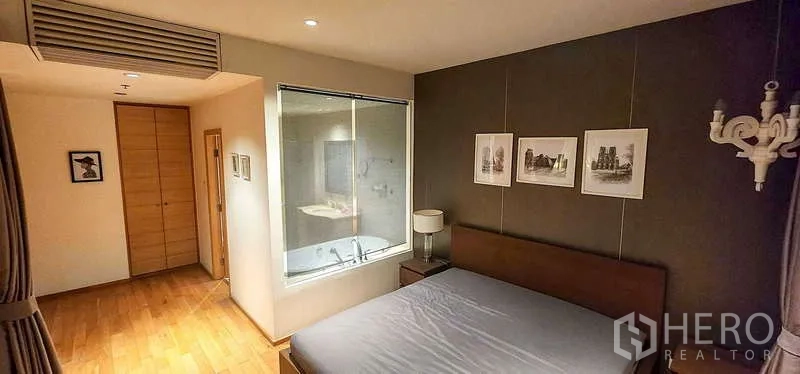 Condominium for sale in Sathon, Bangkok - Bedroom with wood floors, feature wall and interior window looking into the bathroom.