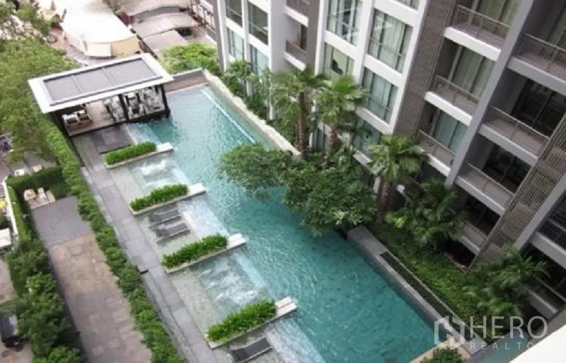 公寓 出租在Watthana, Bangkok - 公寓度假式泳池鸟瞰图，设水中躺椅与葱郁景观。