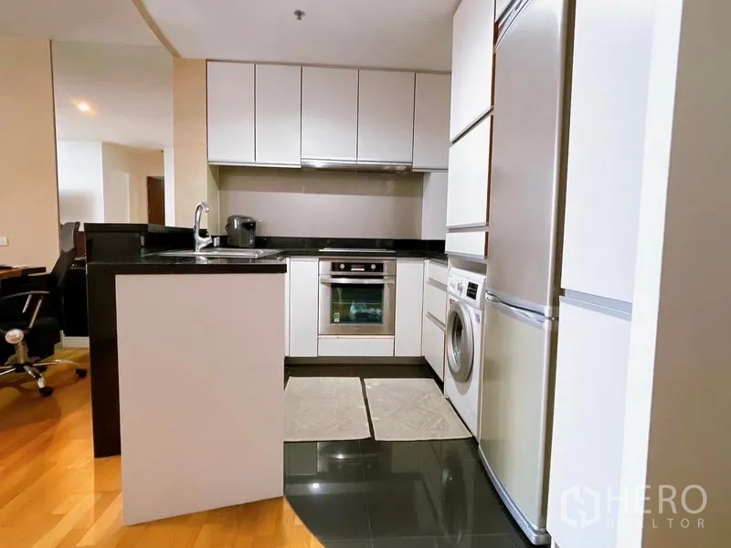 Condominium for rent or sale in Sathon, Bangkok - Compact L-shaped kitchen with black stone countertops, built-in oven, refrigerator and washing machine.