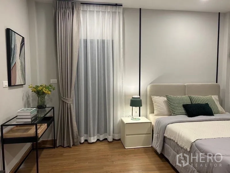 Detached House for rent or sale in Bang Phli, Samut Prakan - Cozy bedroom with upholstered bed, bedside table, soft drapes and wall art.