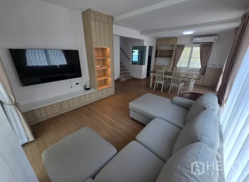 Detached House for rent in Bang Phli, Samut Prakan - Living room with large sectional sofa, feature TV wall and adjacent dining space.