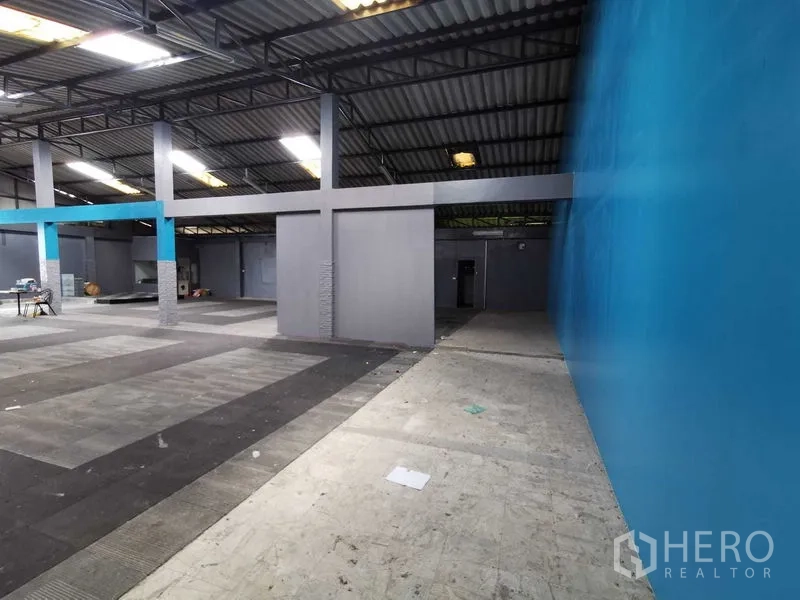 货栈 出租在Nonthaburi - 沿蓝色墙面的通道，通往开阔仓库与灰色隔间。