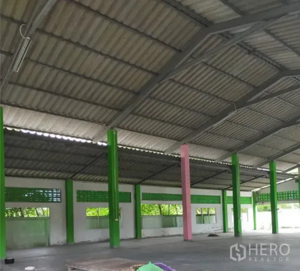 工厂 出租或出售在Samut Prakan - 工厂内部空间开阔，高金属屋顶，绿色立柱、通风砖与水泥地面。