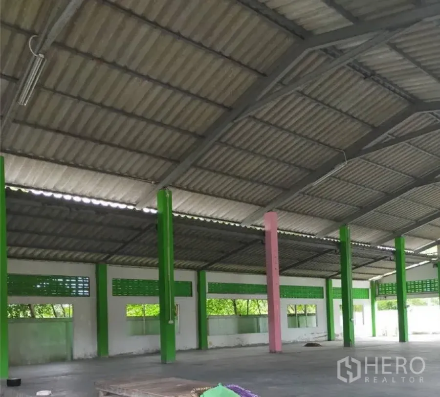 工厂 出租或出售在Samut Prakan - 工厂内部空间开阔，高金属屋顶，绿色立柱、通风砖与水泥地面。