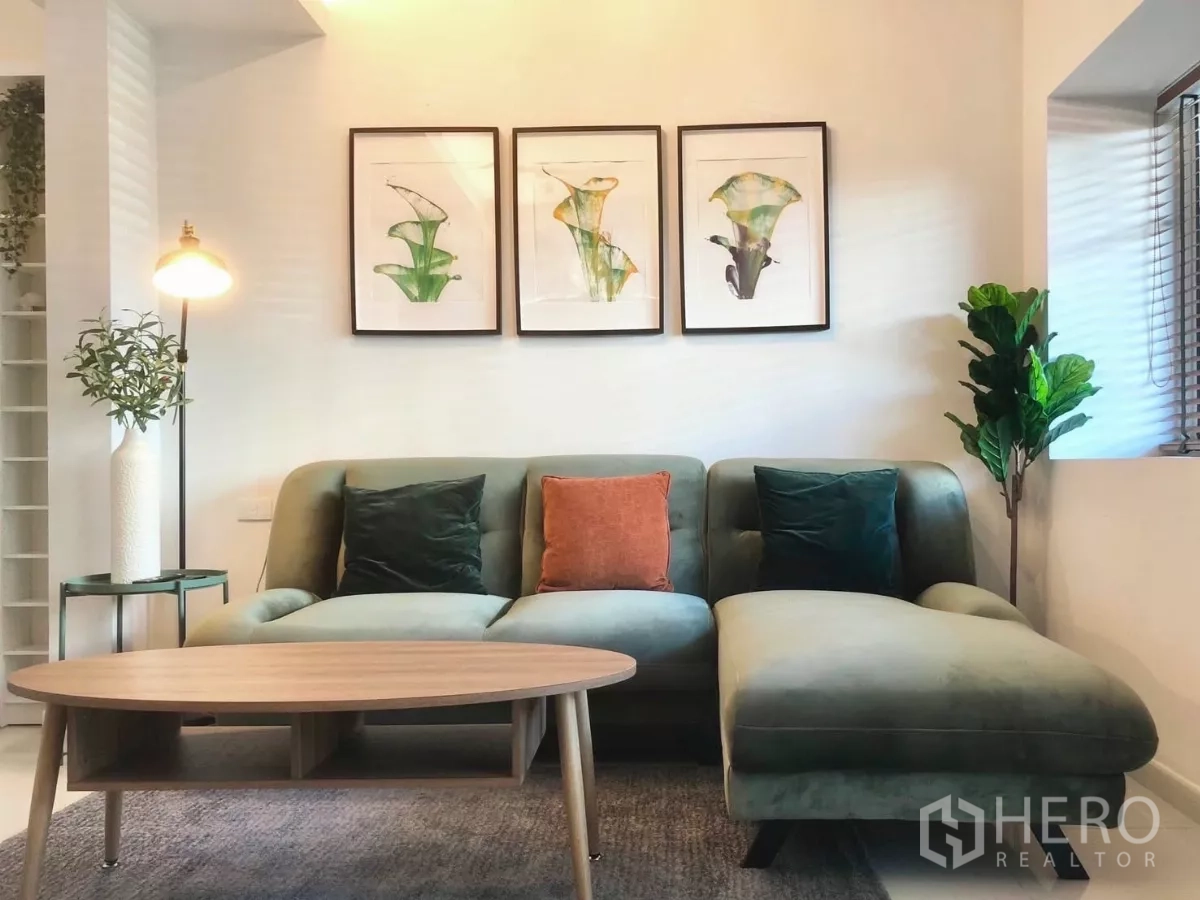 Townhouse for rent or sale in Bang Phli, Samut Prakan - Bright living room with green sectional sofa, wooden coffee table, and framed botanical artwork.