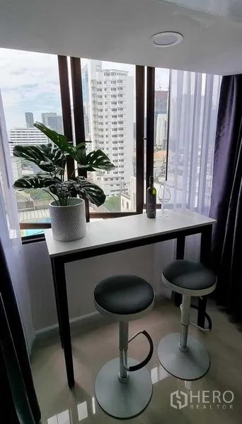 公寓 出租在Khlong Toei, Bangkok - 窗边吧台配两张高脚椅与绿植，可观赏城市天际线。