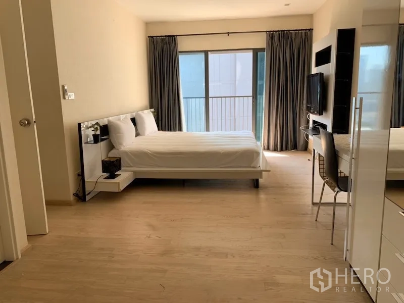 คอนโด ให้เช่าในKhlong Toei, Bangkok - ห้องนอนสว่าง เตียงสีขาว พื้นไม้ ประตูกระจกบานเลื่อนออกสู่ระเบียง พร้อมทีวีติดผนังและโต๊ะทำงาน