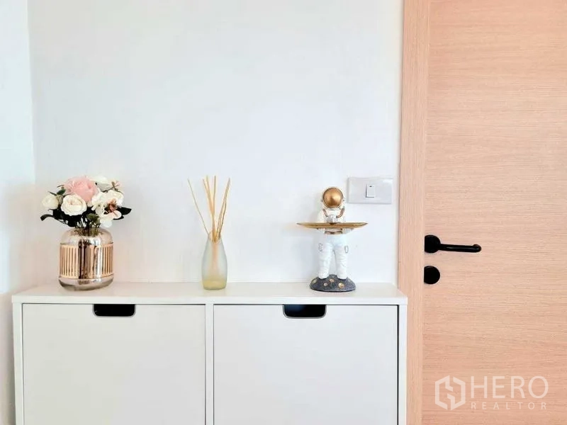 คอนโด ขาย - ตู้คอนโซลทางเข้า แจกันดอกไม้ ก้านกระจายกลิ่น และของตกแต่ง ข้างประตูไม้สีอ่อน