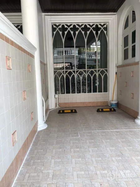 Townhouse for rent in Khlong Toei, Bangkok - Covered carport with tiled floor and tall gothic‑style window grille.