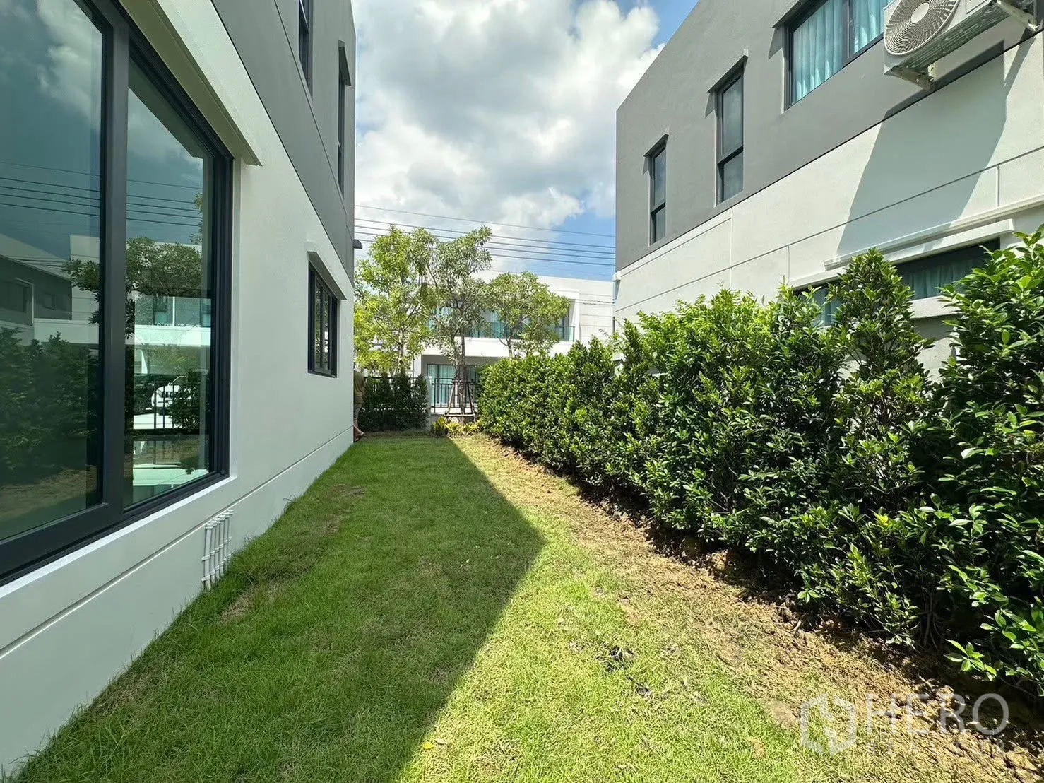 Detached House for rent in Bang Phli, Samut Prakan - Side lawn with trimmed hedges between two modern houses and large windows.