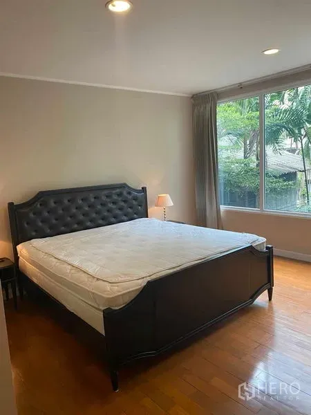 Condominium for rent in Pathum Wan, Bangkok - Master bedroom with tufted bed, wood flooring and corner window facing trees.