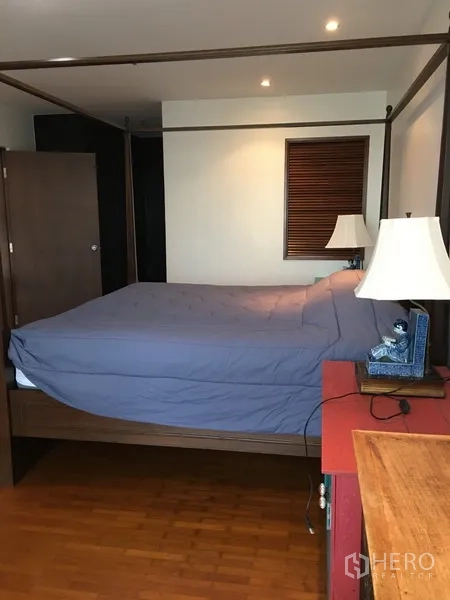 Condominium for rent in Pathum Wan, Bangkok - Bedroom with four-poster bed, bedside lamp, and wooden flooring.