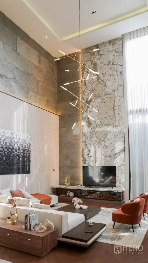 独立式住宅 出租或出售在Bang Kapi, Bangkok - 挑高客厅配大理石背景墙、设计感吊灯与电视壁炉台。