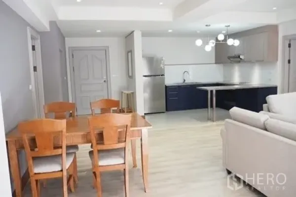 Condominium for rent in Pathum Wan, Bangkok - Dining area with wooden table and chairs beside the open kitchen.