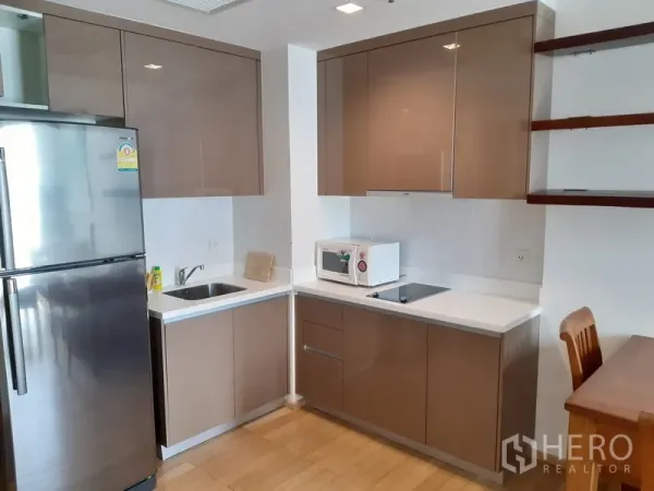 Condominium for rent in Khlong Toei, Bangkok - Modern corner kitchen with glossy cabinets, stainless fridge, cooktop and microwave.
